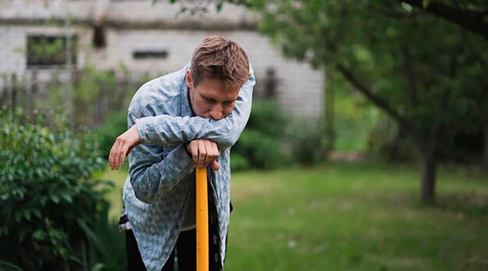 Personne appuyée sur une pelle dans un jardin, illustrant les erreurs à éviter lors de l’entretien d’un mélange terre-pierre en été.